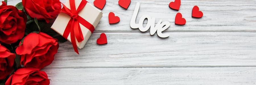 Cup of tart and ruby red hibiscus tea on valentines background with red roses, a gift box, and 'love' cutout | tea + munchies