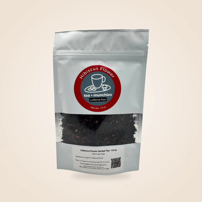 A white stand-up pouch of Hibiscus Flower Caffeine Free Herbal Tea by tea + munchies, featuring a clear window showing dark herbal tea leaves inside, set against a solid light beige background.